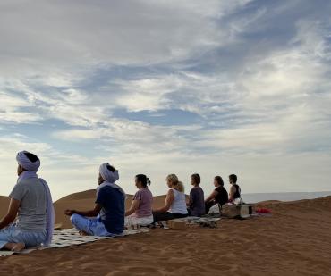 Groupe en méditation au crépuscule pendant une retraite de yoga dans le désert du Maroc
