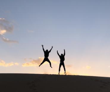 Voyageurs sautant sur une dune au coucher du soleil dans le désert du Maroc lors d’un circuit nomade de 5 jours